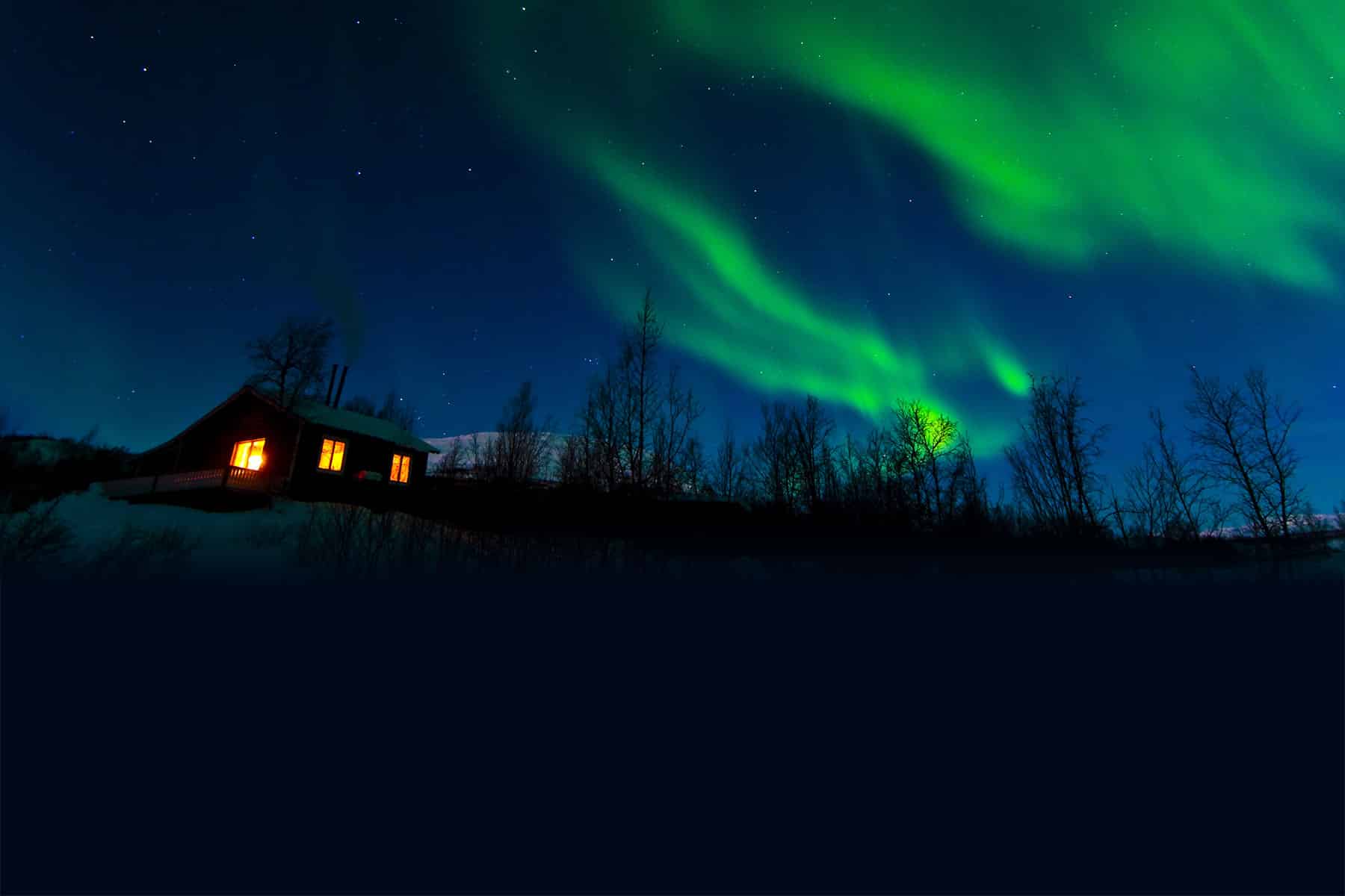 Alaskan cabin lit up at night with Northern Lights